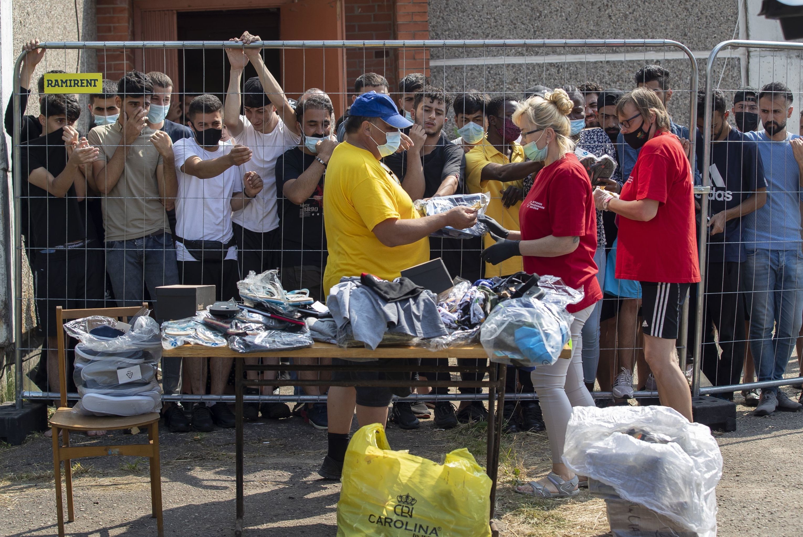 Литовцы продают вещи мигрантам, стоящим за забором в лагере беженцев в селе Веребежай, Литва