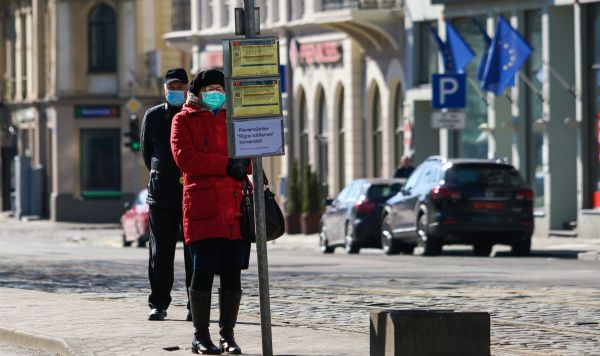 Прохожие в защитных масках на остановке общественного транспорта в Риге. В Латвии из-за коронавируса объявлено чрезвычайное положение