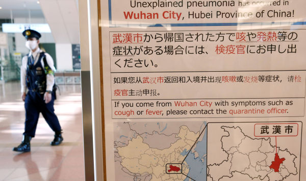 Полицейский в маске проходит мимо уведомления о вспышке коронавируса в Ухане, Китай, в зале прилета аэропорта Ханэда в Токио, Япония, 20 января 2020 года