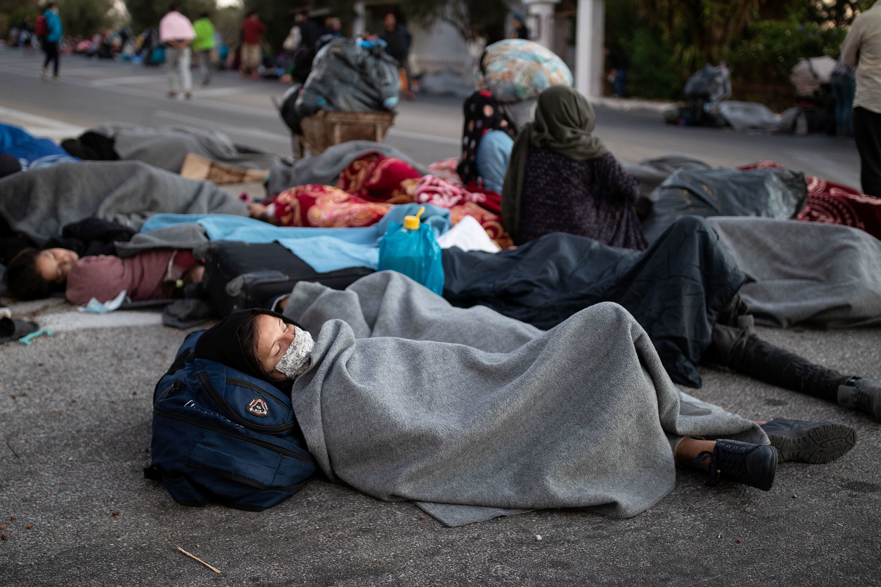 Беженцы и мигранты спят на дороге после пожара в лагере Мориа на острове Лесбос