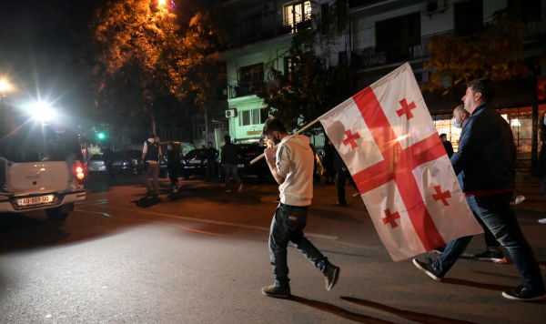 Мужчина несет грузинский флаг во время митинга после объявления предварительных результатов парламентских выборов в Тбилиси, Грузия