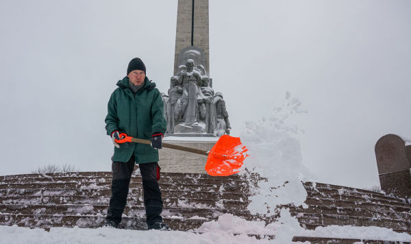 Мужчина убирает снег у памятника Свободы в Риге