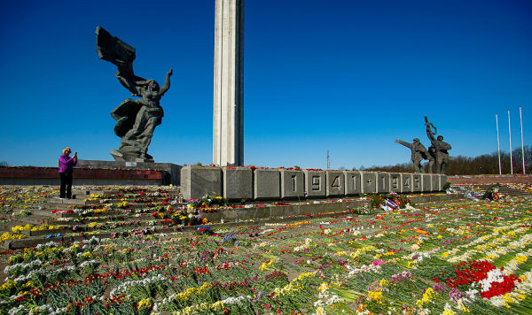 Женщина фотографирует цветы, разложенные у памятника Освободителям Риги