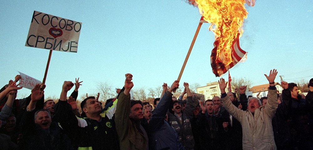 Сербские демонстранты сжигают американский флаг, протестуя против авиаударов НАТО по Югославии у посольства США в Скопье, 25 марта 1999 года